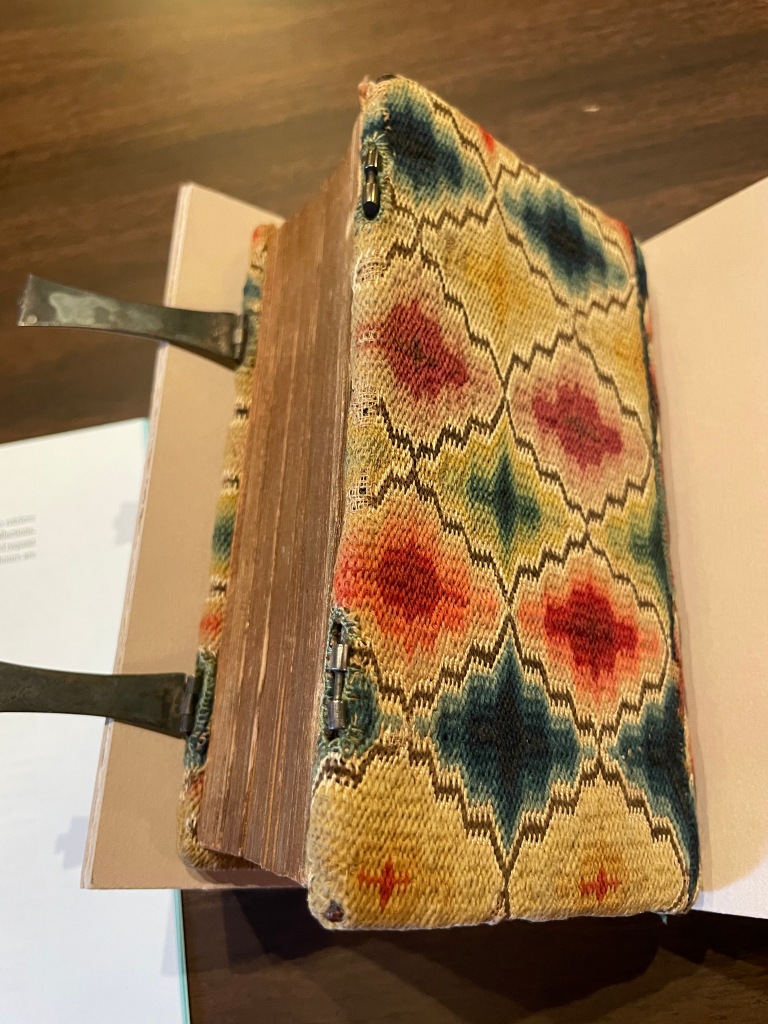A hand-embroidered cover on a Bible dated to 1743, belonging to Mary Sandwith. It's red, green, blue, and yellow on a cream background using flamestitch. 